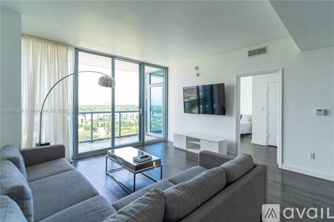 A living room with a grey couch and a flat screen TV mounted on the wall.
