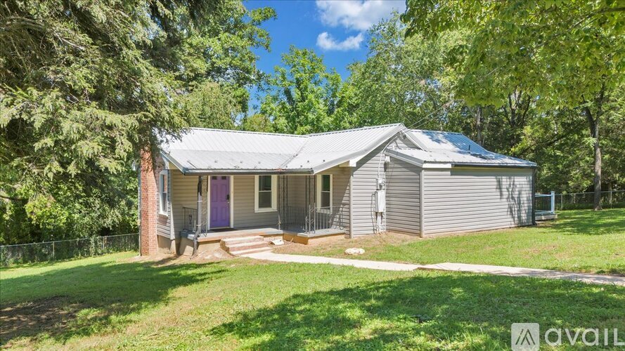 A house with a grey roof and a purple door is surrounded by greenery.