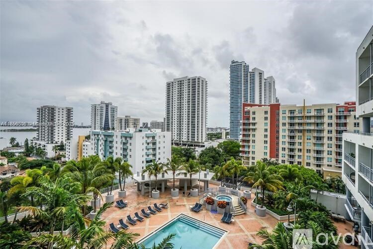 A pool surrounded by chairs and palm trees in front of apartment buildings.