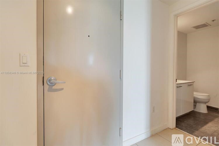 A white door with a silver handle is open to a bathroom.