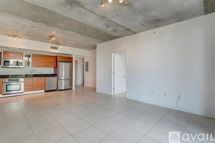 A spacious, empty room with a kitchen area in the background.