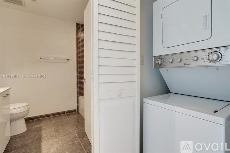 A white washing machine sits next to a white toilet in a small bathroom.