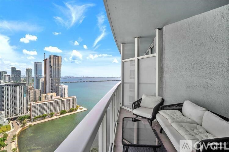 A balcony with a white couch and a table overlooking a city skyline and water.