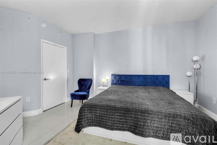 A bedroom with a bed, chair, and a wall-mounted light fixture.