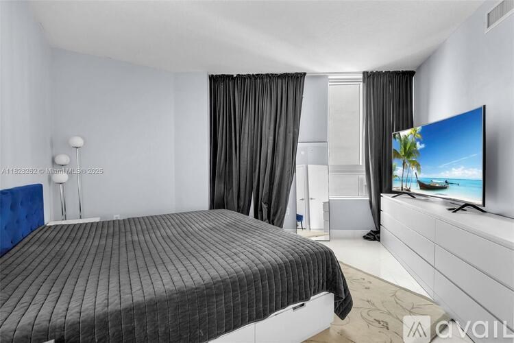 A bedroom with a bed, a television, and a window with curtains.