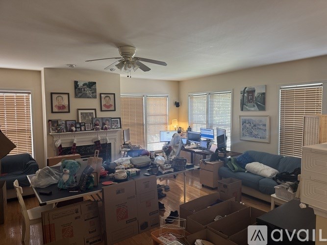 A living room with boxes on the floor and a fan on the ceiling.