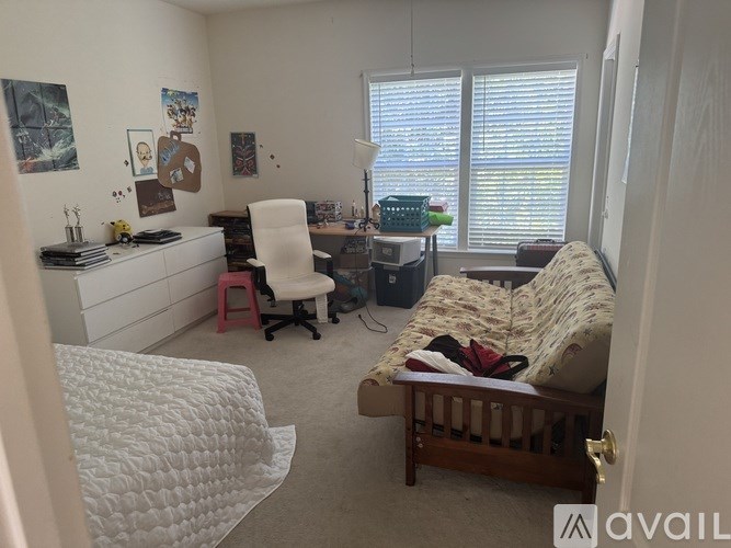 A bedroom with a white bed, a desk with a chair, and a window with blinds.