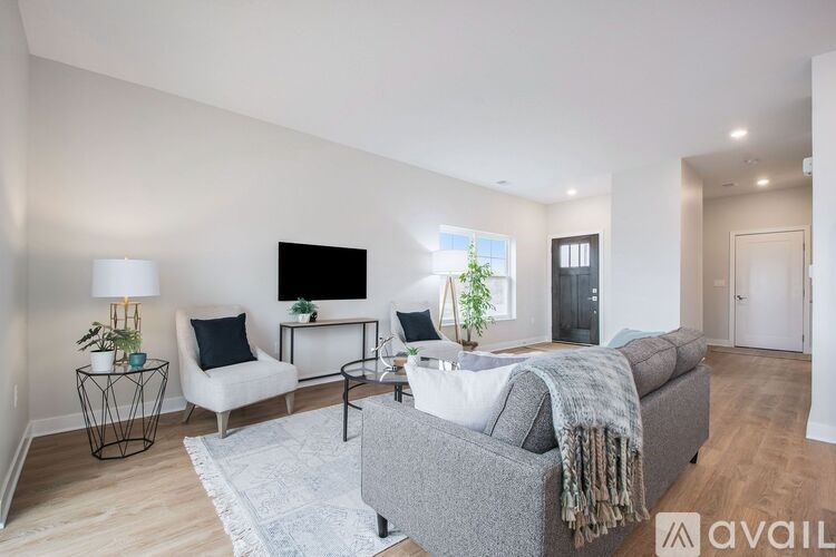 A modern living room with a grey sofa, a white armchair, a black TV, and a wooden floor.