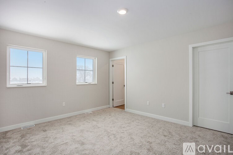A room with a carpeted floor, two windows, and a door.