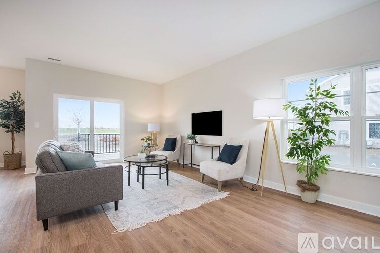 A living room with a grey couch, a black coffee table, a white chair, and a TV on the wall.