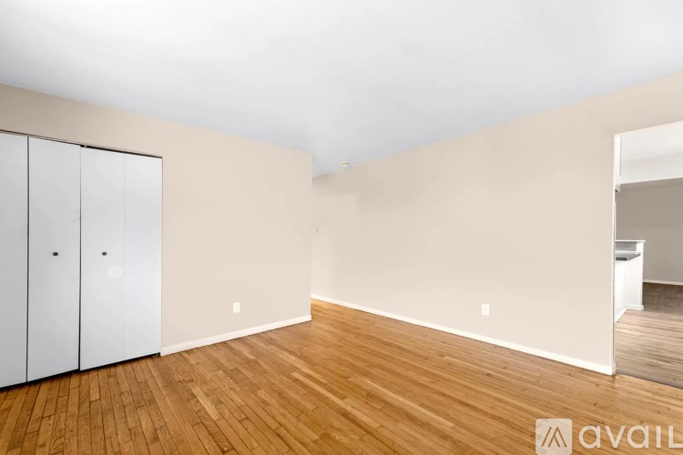 A room with wooden floors and white walls, with a white closet on the left.