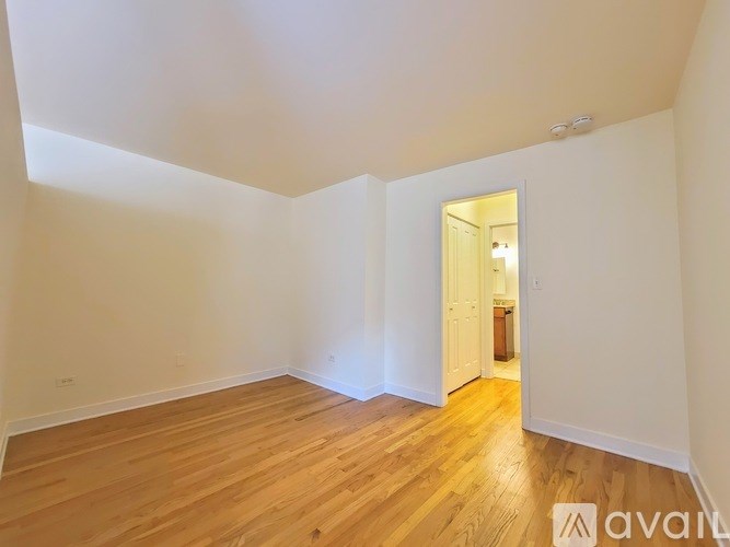 A room with wooden flooring and white walls, with a doorway leading to another room.
