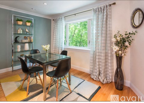 A glass dining table with four chairs and a vase of flowers on a rug in front of a window.