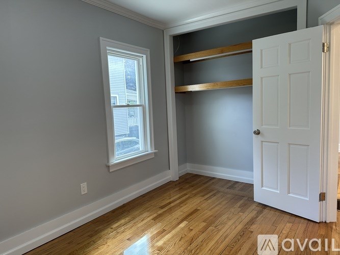 A room with a white door, a window, and a wooden floor.