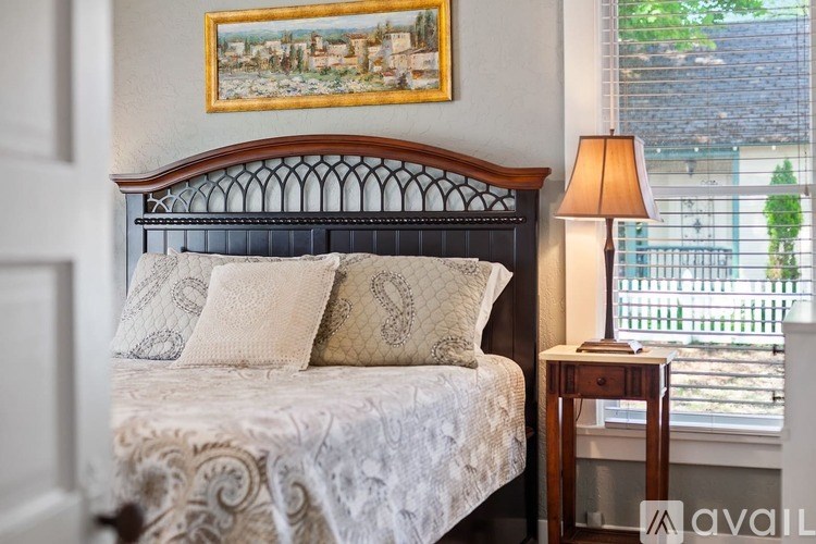 A bed with a white comforter and a brown headboard with a painting on the wall above it.
