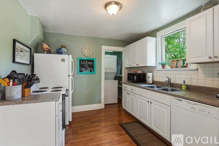 A kitchen with white appliances and cabinets, a chalkboard sign on the wall, and a window with a view of trees.