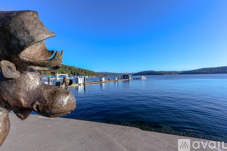 A large dinosaur head sculpture is in the foreground of a body of water with a dock and boats in the background.