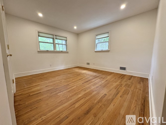 A room with wooden flooring and two windows.