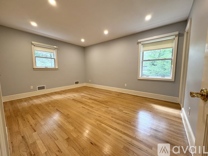 A room with wooden flooring and two windows.