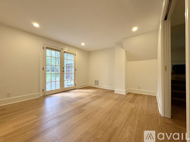 A spacious room with wooden flooring and a large window.
