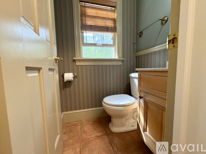 A bathroom with a toilet, a window with blinds, and a wooden cabinet.