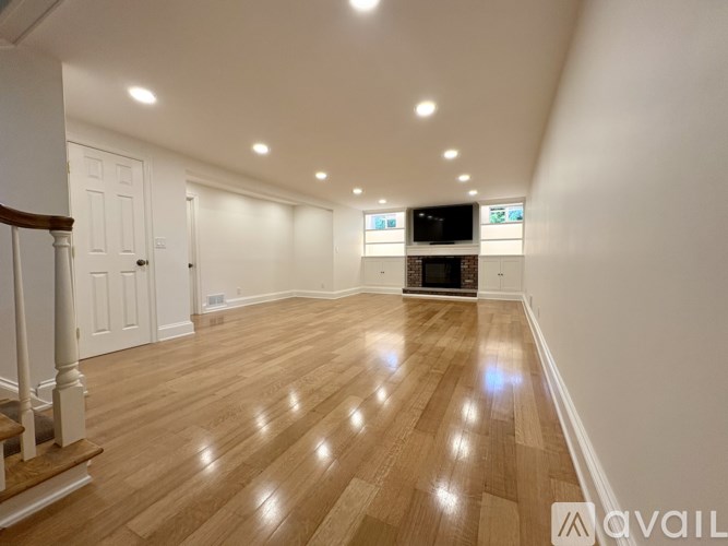 A spacious room with wooden flooring and a staircase on the left.