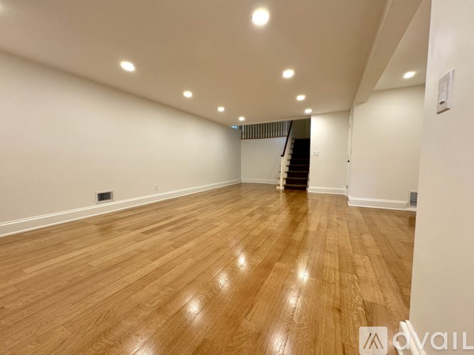 A room with wooden flooring and a staircase in the background.