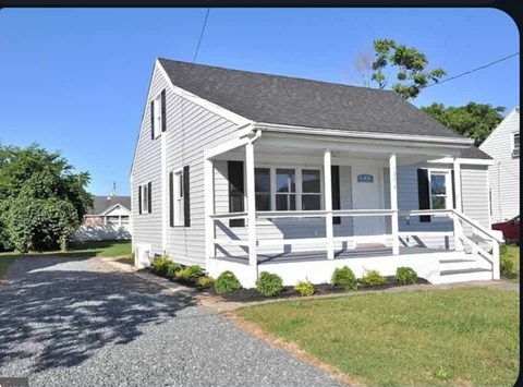 A small white house with a grey roof and a porch.