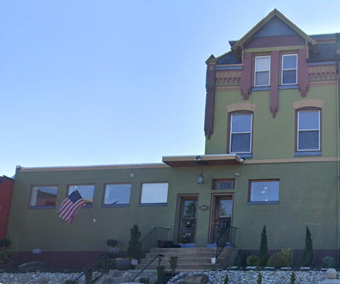 A green house with a red door and a flag on the wall.