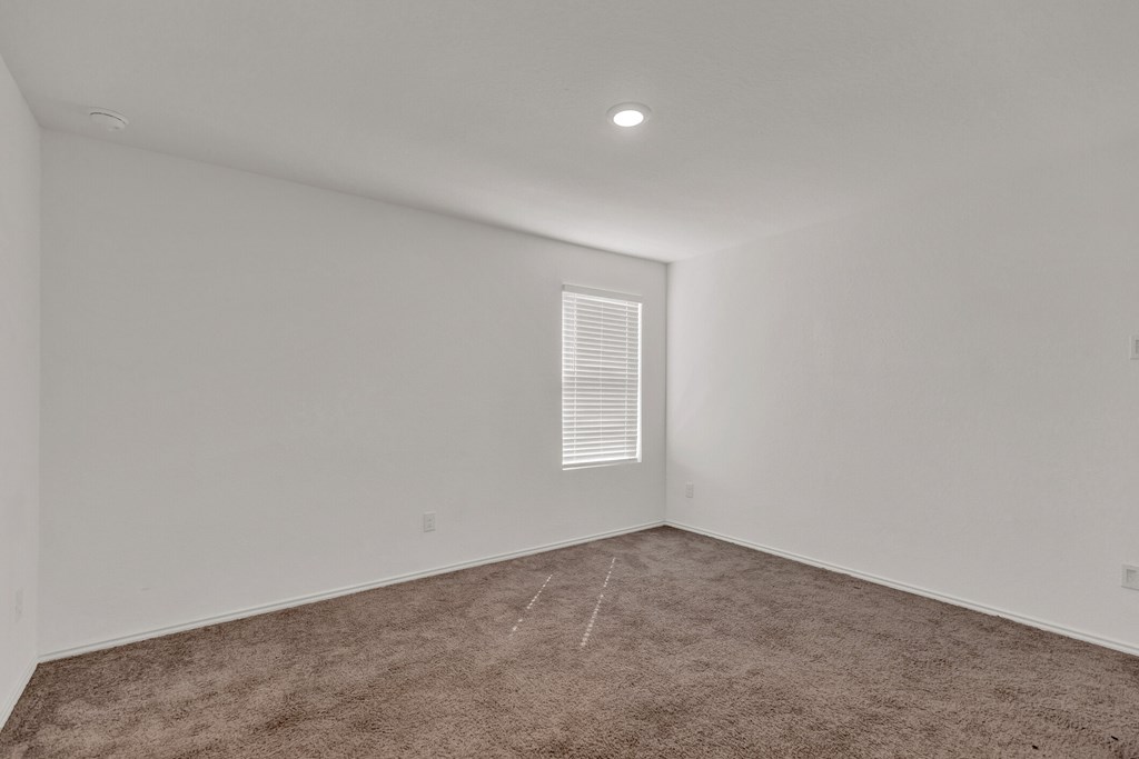 A room with a carpeted floor and a window with blinds.