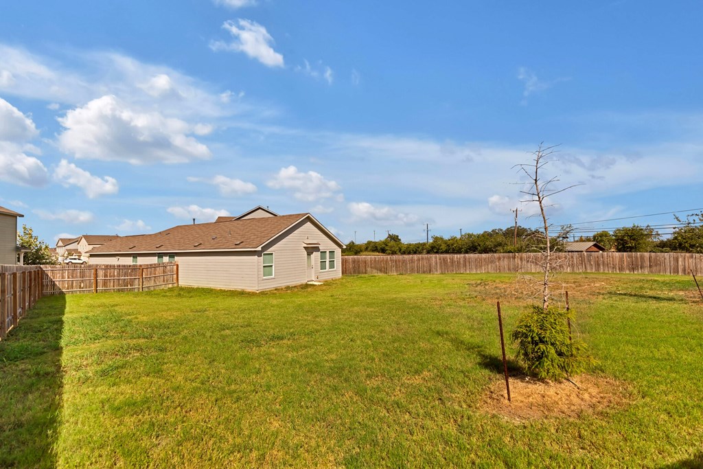 A small house with a fence and a tree in the backyard.