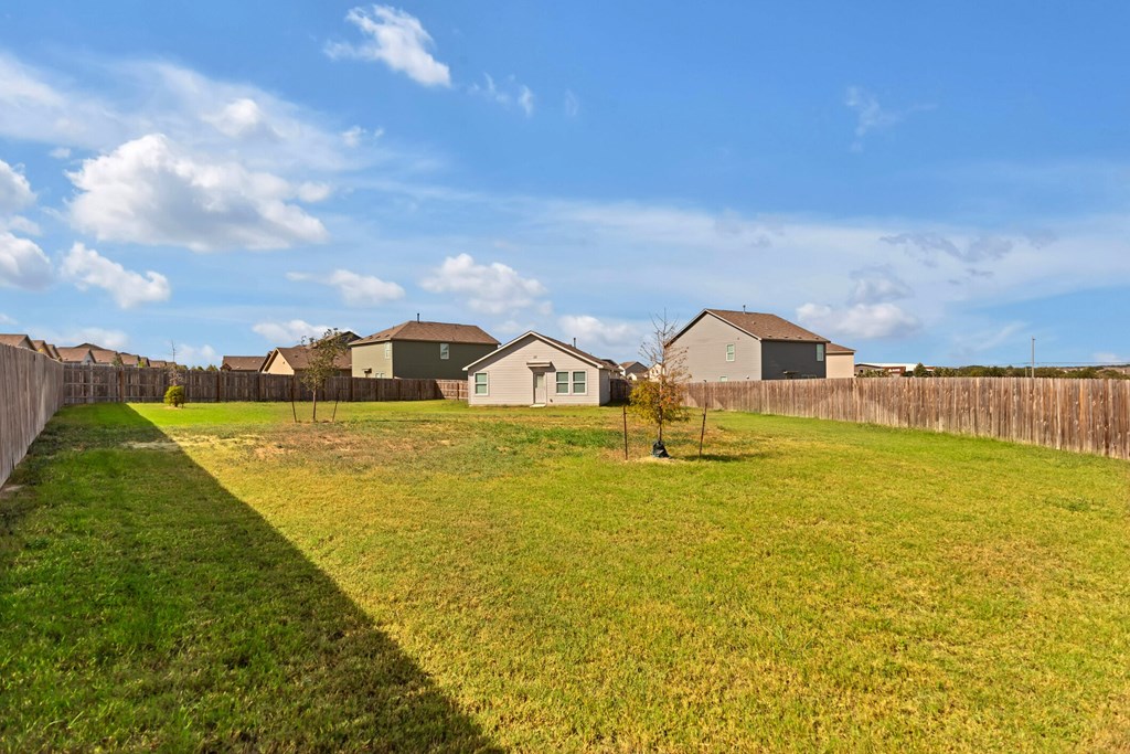 A grassy field with a fence and houses in the background.