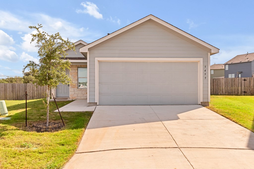 A house with a white garage door and a tree in front.