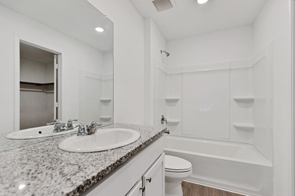 A white bathroom with a granite countertop and a white bathtub.