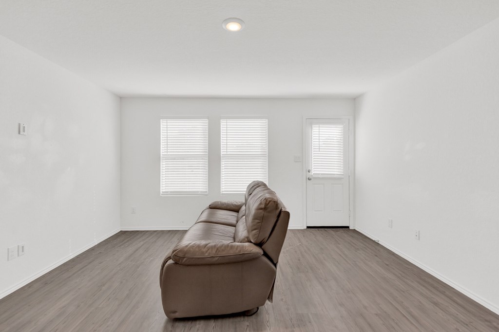 A brown couch is in the middle of a white room with wooden floors and a white door.
