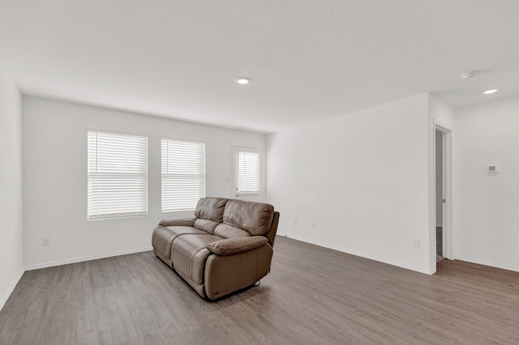A brown leather sofa sits in a spacious room with wooden floors and white walls.