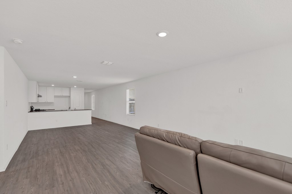 A living room with a brown couch and a kitchen in the background.