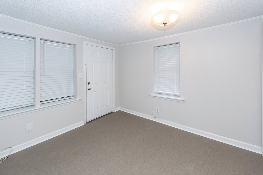 A white room with a door, a window with blinds, and a light on the ceiling.