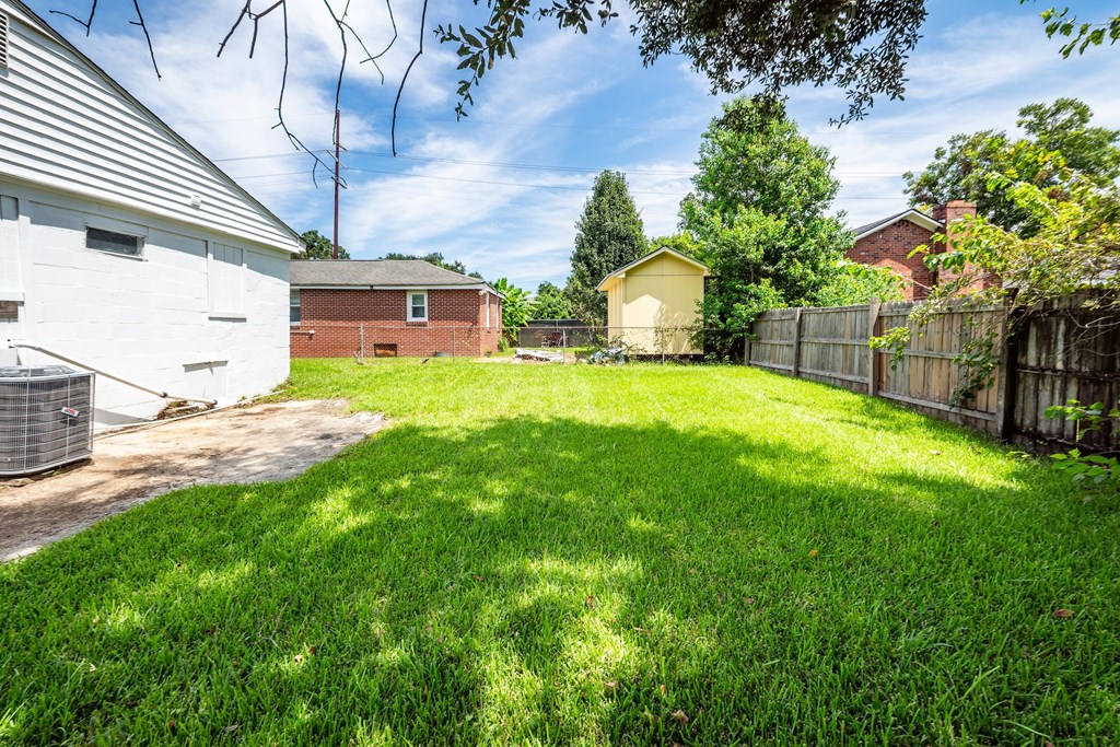 A backyard with a white house and a green lawn.