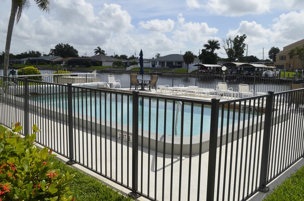A pool surrounded by a black fence with a small red flower in the foreground.