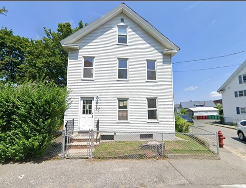 A white house with a grey roof and a grey fence.
