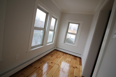 A room with wooden floors and three windows.