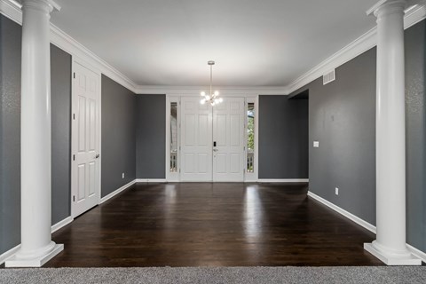 A spacious hallway with white columns and a chandelier.