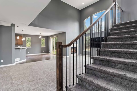 A staircase with a wooden handrail leads to a bright room with a large window.