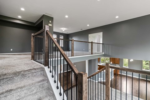 A staircase with a wooden handrail and black metal balusters leads to a second floor.