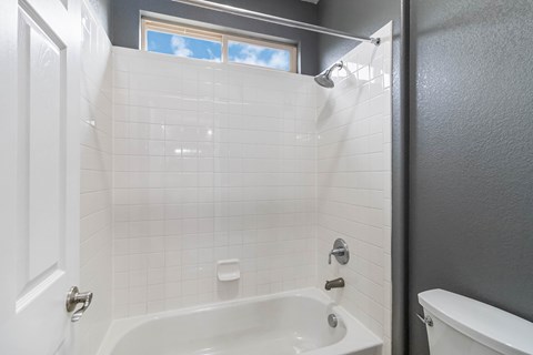 A white bathtub with a shower head and a window in the shower.