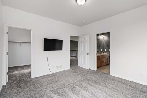 A room with a grey carpet and a flat screen TV mounted on the wall.