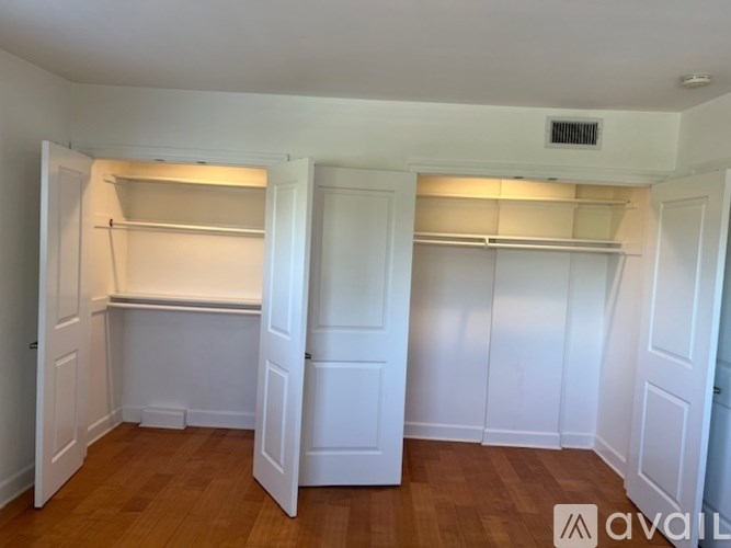 A room with white walls and wooden floors, featuring two white closets with shelves.