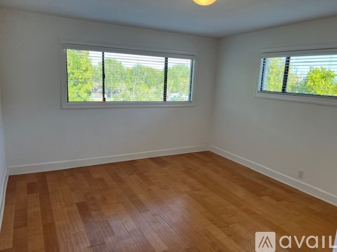 A room with wooden flooring and two windows.