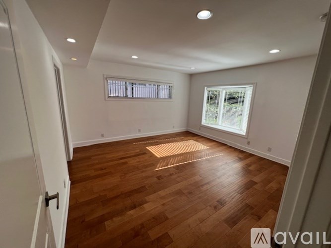 A room with wooden flooring and two windows.